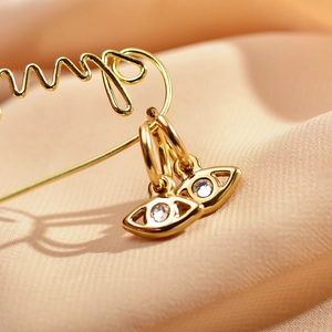 Minimalist gold eye earrings with sparkling zircon drop design on pink silk background