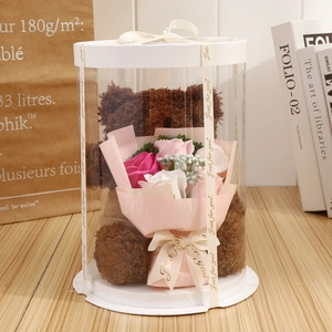 Close-up of a brown plush teddy bear holding soap roses in a transparent gift box