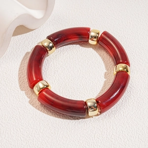 Close-up of red marble acrylic tube beads with gold metal spacers on white stone surface