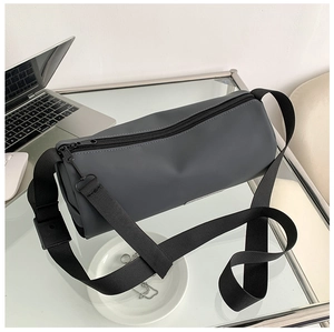 Détail du sac cylindrique gris foncé avec bandoulière réglable sur un bureau vitré