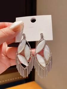 Macro shot of silver hollow oval earrings with long fine chain tassels and faux shell inlays