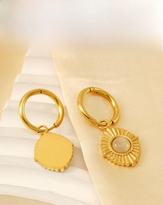 Détail de boucles d'oreilles soleil vintage avec pierre œil de chat sur fond beige