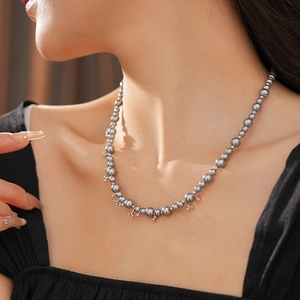 Close-up of elegant grey pearl choker necklace featuring a delicate cross pendant on model