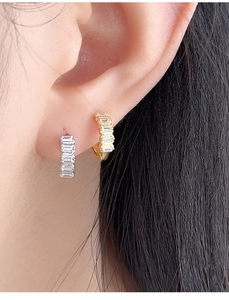 Close-up of gold and silver mini huggie earrings with baguette-cut zircons on ears