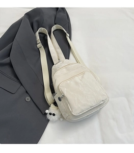 Dettaglio della borsa pettorale bianco crema con cerniere multiple e ciondolo in peluche