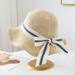 Detail of beige straw hat featuring elegant white lace ribbon and a large bow tie design