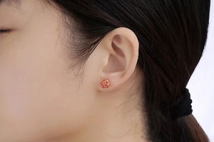 Close-up of gold-plated rose earring with red enamel on a female model