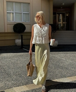 Close-up of white pleated sleeveless top and satin midi skirt on a street model