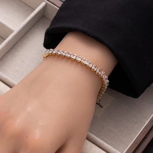 Close-up of a golden tennis bracelet with princess cut zircons on a model wrist