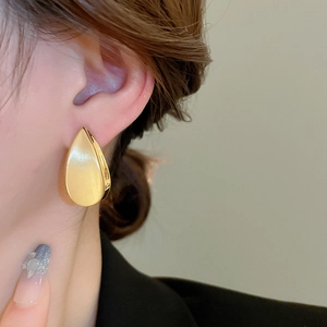 Dettaglio di grandi orecchini a goccia placcati in oro 18k con lucentezza metallica e curve