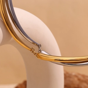 Detail of two-tone gold and silver bamboo style necklaces on a beige display stand