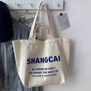 Detail of off-white canvas tote bag with blue bold text hanging in a lifestyle setting