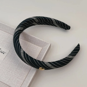 Détail d'un serre-tête rayé avec pendentif coeur doré sur un plateau de présentation gris
