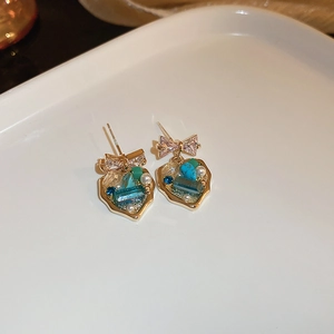 Vue macro de boucles d'oreilles nœud doré avec cœurs en cristal bleu et vert