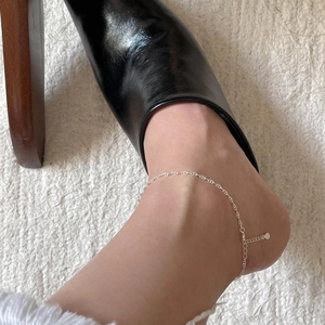 Close-up of a minimalist S925 sterling silver anklet chain worn on the ankle with black shoes