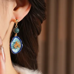 Vintage gold and emerald green floral drop earrings with blue enamel petals on a model