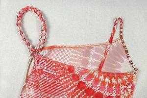 Detail of vibrant mesh fabric with red and orange prints and asymmetric braided strap