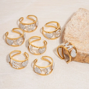Close-up of golden adjustable open rings with sparkling crystal letters and heart charms