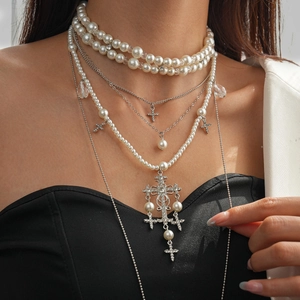 Detail of layered faux pearl and rhinestone cross pendant necklace set on a model
