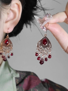 Close-up of vintage red teardrop tassel earrings with intricate filigree metalwork