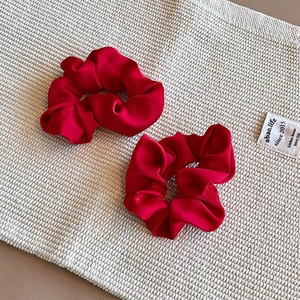 Close-up of two vintage red satin scrunchies featuring high gloss and elegant textures