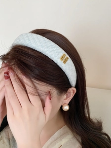 Dettaglio di cerchietto in tweed azzurro con logo in metallo dorato indossato da modella