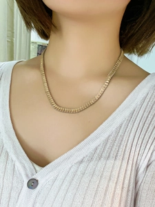 Detail of a minimalist gold square-link chain necklace worn by a model in soft lighting