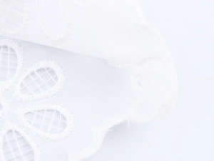 Detailed macro view of white floral lace fabric with intricate embroidery and cutout design