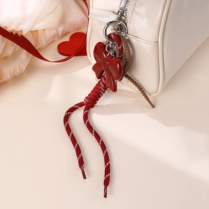 Detail of red bow charm with woven cord attached to a beige bag's zipper pull