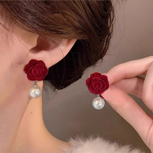 Dettaglio di orecchini a fiore rosso con perla e morbida texture in velluto su modella