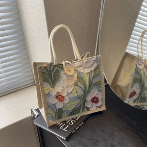 Detailed relief of white flowers on a linen handbag with woven rope handles and yellow button