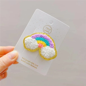 Close-up of plush rainbow hair clip with gold glitter edges for girls on white card
