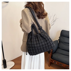 Detail of a black quilted puffer tote bag with knotted shoulder strap worn by a model