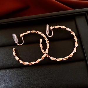 Detail of rose gold geometric faceted hoop clip-on earrings on black leather texture