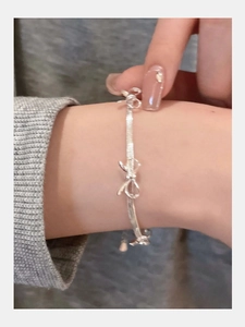 Close-up of a silver bow knot bracelet featuring a sleek snake chain on a woman wrist