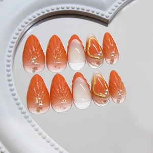Orange and white press-on nails with 3D shell texture, pearls, and gold-painted accents