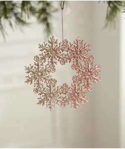 Macro shot of rose gold glitter snowflake ornament hanging on a lush green Christmas tree branch