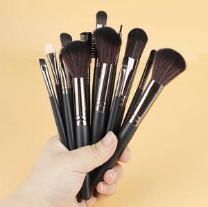 Détail de mains tenant des pinceaux de maquillage aux poils denses et manches noirs mats
