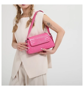 Detailed side view of bright pink croc-embossed handbag worn by a model in light tones