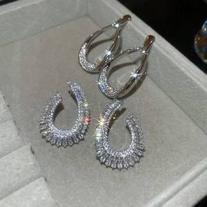 Macro detail of teardrop and U-shape zircon earrings on a grey velvet jewelry tray