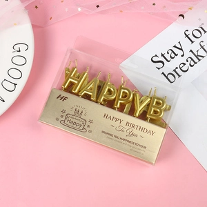 Close-up of golden metallic HAPPY BIRTHDAY letter candles on a soft pink background