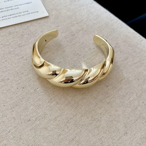 Macro shot of gold twisted cuff bracelet with irregular texture on beige linen background