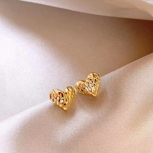 Close-up of golden heart earrings with hammered texture on soft silk fabric background