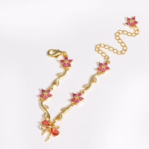 Detail of gold bracelet with pink zircon flowers and a red bow pendant on white background