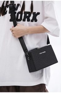Detail of black ostrich-textured crossbody box bag with wide strap and silver hardware