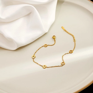 Detail showing gold link bracelet with five gear-shaped charms on a ceramic plate