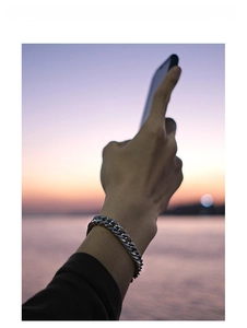 Close-up of polished silver stainless steel curb chain bracelet worn on wrist at sunset