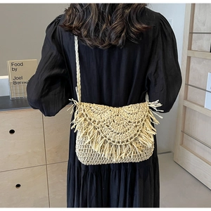 Detail of hand-woven straw crossbody bag with tassel and semicircular flap design