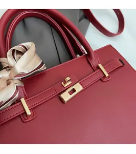 Detailed close-up of dark red handbag with gold clasp lock and decorative silk scarf