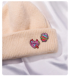 Close-up of pink enamel heart and love potion brooches pinned on a beige knitted hat